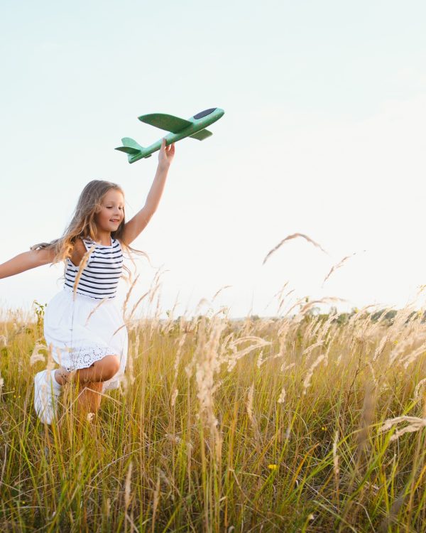 Happy kid with toy plane is playing at sunset
